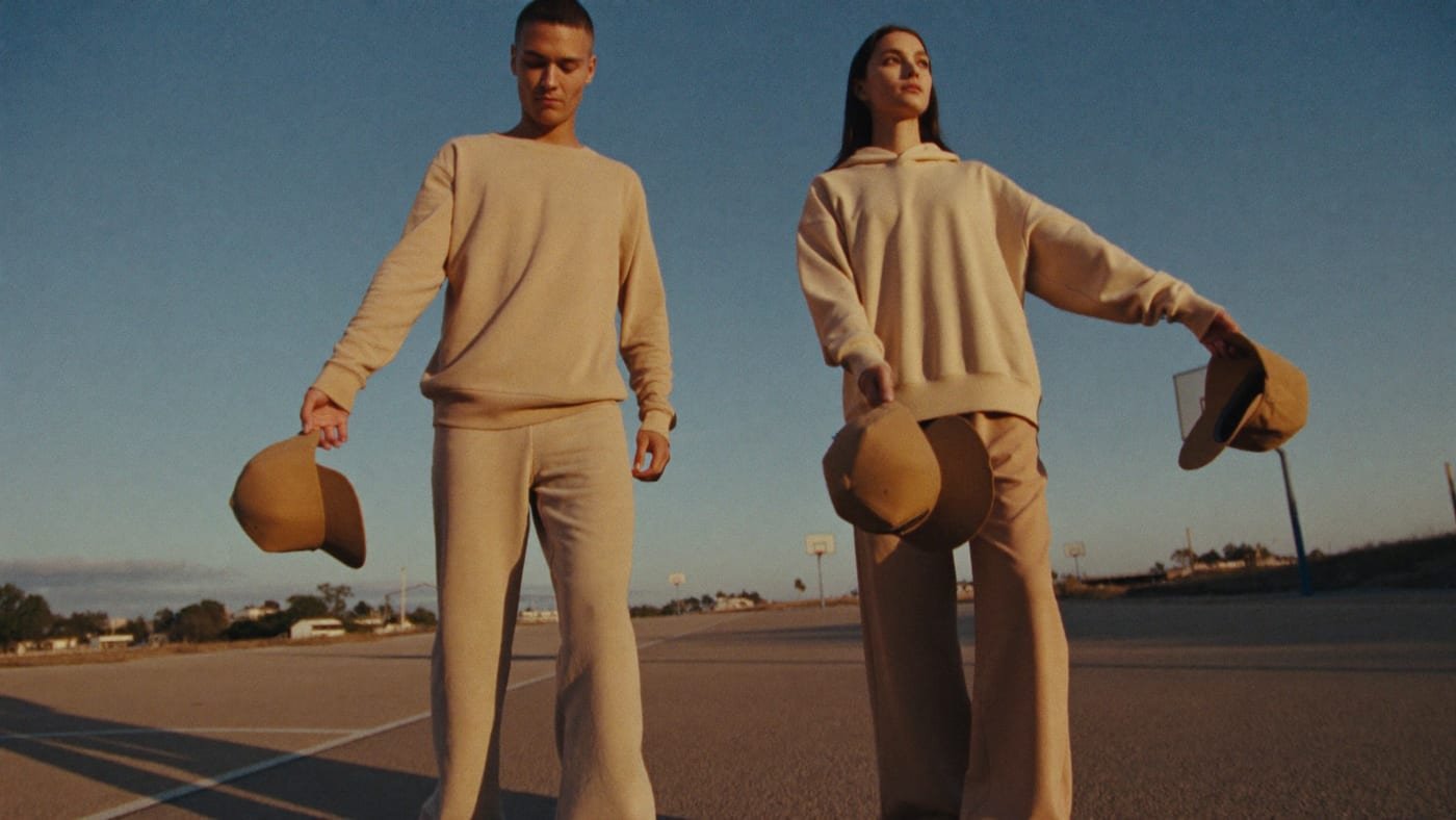 Dupla de modelos numa quadra ao entardecer segurando os bonés do Drop 03
